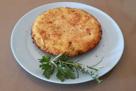 Frittata di cous cous dorata e croccante, guarnita con erbe aromatiche fresche su un piatto azzurro.
