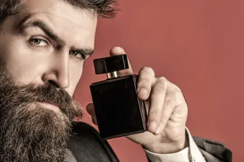 Mężczyzna z brodą trzyma czarną buteleczkę perfum, zastanawiając się, gdzie psikać perfumy, by podkreślić swój styl.