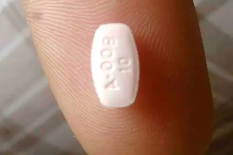 Biała tabletka z oznaczeniem "A-009 10" na palcu. Może to być lek, np. Abilify, pomagający w leczeniu schizofrenii.