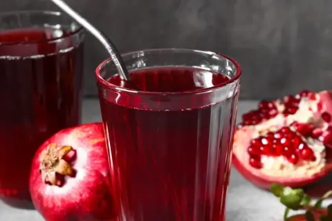 Szklanka z sokiem z granatów, obok owoców. Czy sok malinowy obniża ciśnienie? Ten napój może pomóc.