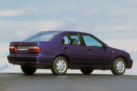 Fioletowy Nissan Almera z lat 90. stoi na tle błękitnego nieba.