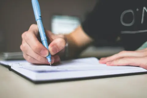 Dłoń pisze niebieskim długopisem w notatniku. Przyszły skrót inżynier tworzy swoje pierwsze notatki.