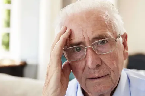 Älterer Mann mit Brille, der sich an die Stirn fasst, wirkt nachdenklich, vielleicht wegen Morbus Korsakow.