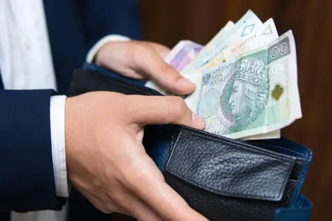 Dłonie wkładają polskie banknoty do portfela. Czy to efekt najlepiej płatnych zawodów?