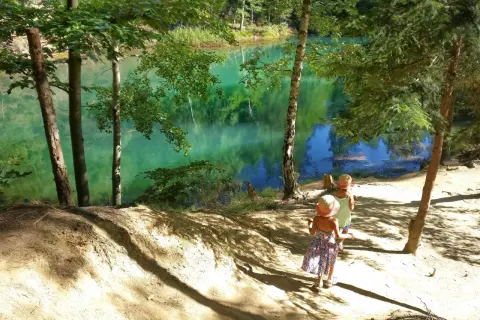 Dwie dziewczynki w słomkowych kapeluszach idą ścieżką nad turkusowe jezioro. Wspaniałe atrakcje dla dzieci Dolny Śląsk czekają!