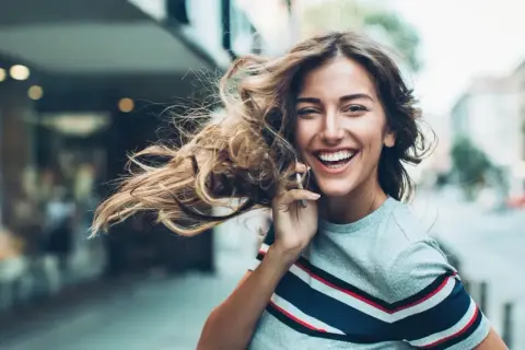 Lachende Frau telefoniert, ihr Haar weht im Wind. Sie genießt ihr **iu auslandssemester** in der Stadt.