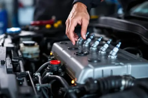 Mécanicien vérifiant les bougies d'allumage d'un moteur essence. Si votre voiture broute en roulant, cela peut venir de là.