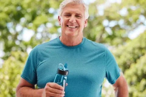 Homme souriant tenant une gourde, prévenu des conséquences de la déshydratation sur le cerveau.