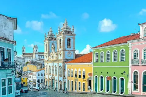 Calles empedradas y coloridas casas coloniales bajo un cielo azul en **Bahía, Brasil**. Una iglesia barroca domina el paisaje.