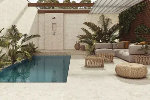 Piscina y zona lounge con sofás y mesas bajas, ducha exterior y plantas exuberantes. El suelo y las paredes lucen un elegante microcemento exterior.