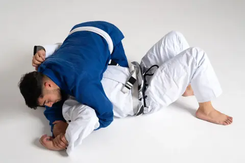 Två män i judodräkter brottas på golvet. En blå och en vit dräkt, en kamp mellan judo vs bjj.