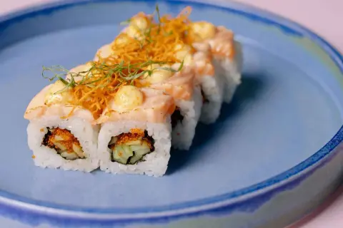 Rolka sushi z łososiem i warzywami na niebieskim talerzu. Czy w ciąży można jeść sushi? To pytanie nurtuje wiele przyszłych mam.