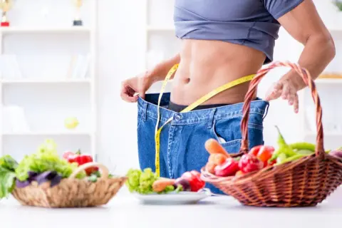 Uomo con jeans larghi e metro, simbolo di successo con dieta ipocalorica. Cesti di verdura fresca in primo piano.