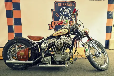 Customowy motocykl z chromowanymi elementami, skórzanym siedzeniem i sakwą, na tle baneru Russian RHC.