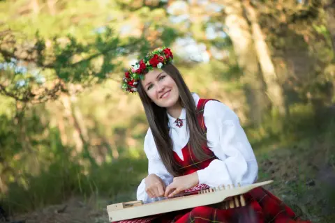 Uśmiechnięta kobieta w wianku i tradycyjnym stroju gra na cymbałach, tworząc piękną polską muzykę ludową.