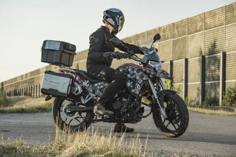 Motocyklista w kasku i czarnej kurtce siedzi na motocyklu Junak RX One 125 z kuframi.