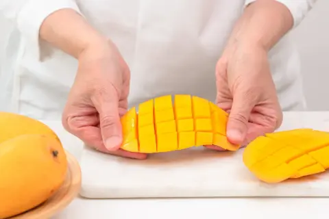 Ręce kroją mango na kostki. Czy koty mogą jeść mango? To pytanie nurtuje wielu właścicieli.