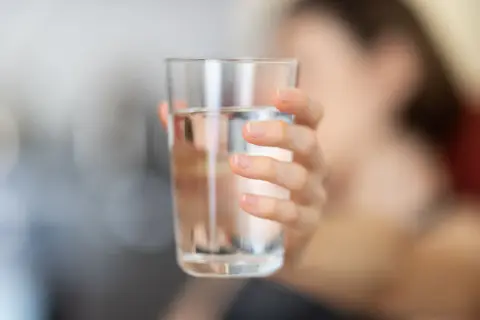 Main d'une personne tenant un verre d'eau. L'eau calcaire peut affecter la santé, mais une hydratation adéquate est essentielle.