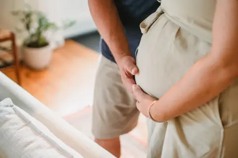 En man håller om sin partners gravida mage. Snart är vattnet gått och bebisen är här.