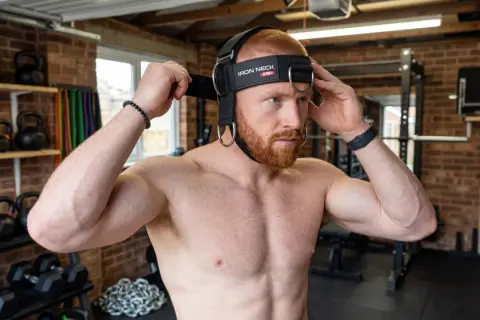 Man adjusting a neck training harness, ready for a workout. This image captures the start of his neck training journey.