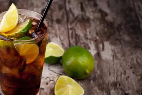 Erfrischender Cuba Libre mit Limettenspalten und Eiswürfeln auf rustikalem Holz. Das Cuba Libre Rezept ist einfach und lecker.