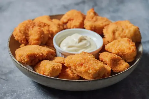 En skål med gyllene, krispiga chicken nuggets och en liten skål med krämig dipp. Perfekt för en snabb och god måltid.