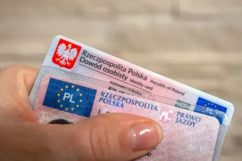 Dłoń trzyma polski dowód osobisty i prawo jazdy. Dokumenty te są niezbędne do poruszania się po drogach, a prawo jazdy bezterminowe daje swobodę na lata.