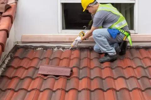 A roofer applies sealant to a shingle roof detail, ensuring a watertight seal around the window.