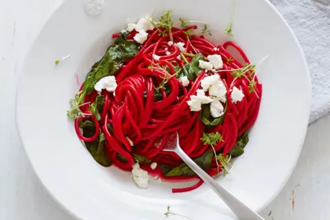 Rote-Bete-Spaghetti mit Spinat, Feta und Kresse auf einem Teller.