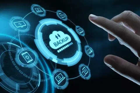Palec dotyka interfejsu chmury z napisem "BACKUP". Ikony komputerów i smartfonów wskazują na kopia bezpieczeństwa danych.