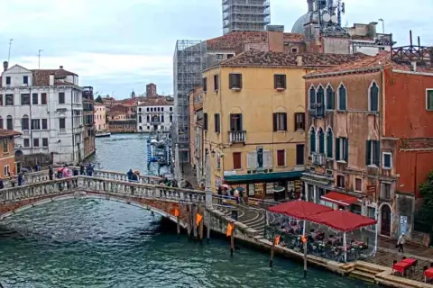 Il ponte delle Guglie attraversa un canale veneziano, circondato da edifici storici e persone che passeggiano.