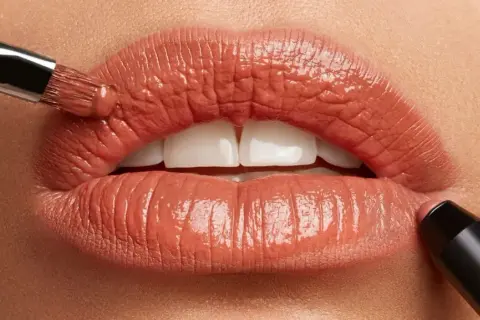Labbra perfette con un tocco di colore. Un pennello applica un prodotto cremoso, mentre un rossetto definisce il contorno.