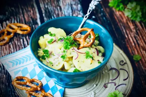 Klassisches Rezept Kartoffelsalat mit roten Zwiebeln und Petersilie, garniert mit einem Brezel.