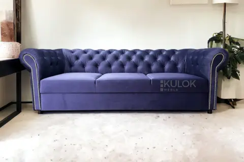 Elegancka, granatowa kanapa chesterfield z pikowanego welwetu, ozdobiona srebrnymi pineskami.