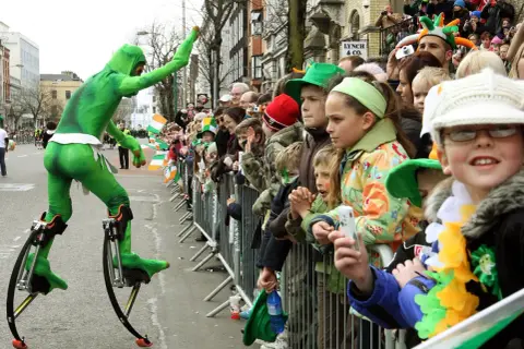 Zielony ludek na szczudłach podczas parady. Gdzie kupić piwo irlandzkie zielone? Może na festynie!
