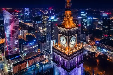 Wieżowiec z zegarami i nowoczesne budynki tworzą magiczny krajobraz warszawa nocą.