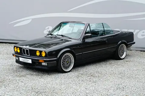 Czarny kabriolet BMW E30 z żółtymi światłami i felgami BBS. Klasyk na drodze.