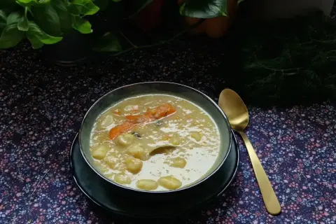 Aromaticzna zupa na żeberkach z kawałkami marchewki i ziemniaków, podana w misce obok złotej łyżki.