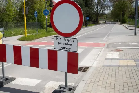 Znak B1 zakazu ruchu z tabliczką "Nie dotyczy pojazdów budowy" na tle drogi z pasami.