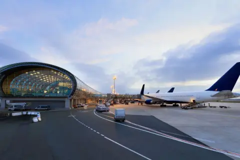 Flugzeuge am Flughafen Paris warten auf den Abflug. Ein modernes Terminalgebäude mit Glasfassade spiegelt den Himmel.