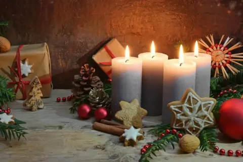 Vier Kerzen, Geschenke und Tannenzweige erzählen die Geschichte von Weihnachten. Lebkuchen und Zimtstangen runden die festliche Szene ab.