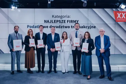 Grupa osób w garniturach i sukienkach odbiera dyplomy na tle ekranu z napisem "Kategoria: Najlepsze Firmy".