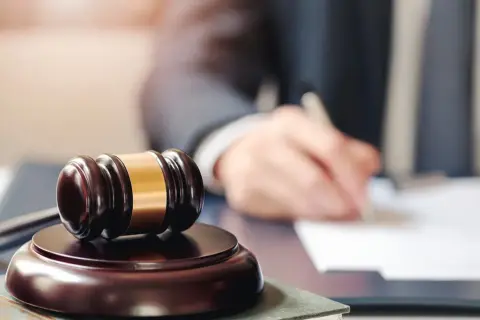 Młotek sędziowski i ręka pisząca dokumenty. Sąd rozstrzyga sprawy, ustalając wynagrodzenie zasadnicze.
