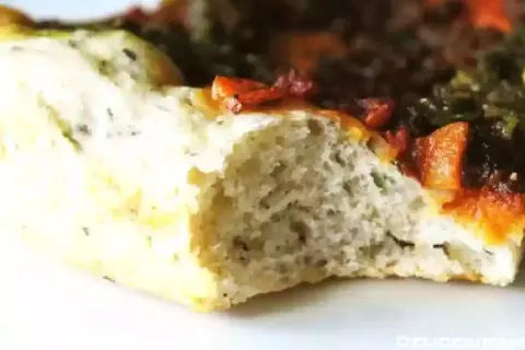 Gros plan sur une tranche de pâte à pizza sans gluten moelleuse, garnie de tomates et d'herbes.
