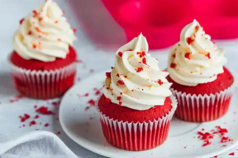 Drei rote Samt-Cupcakes mit cremiger weißer Glasur und roten Krümeln.