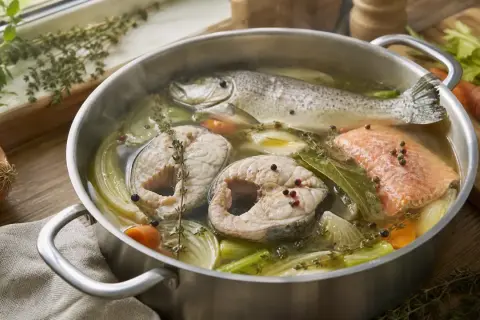 Un poisson entier et des darnes de poisson cuisent dans un court-bouillon avec des légumes et des herbes.