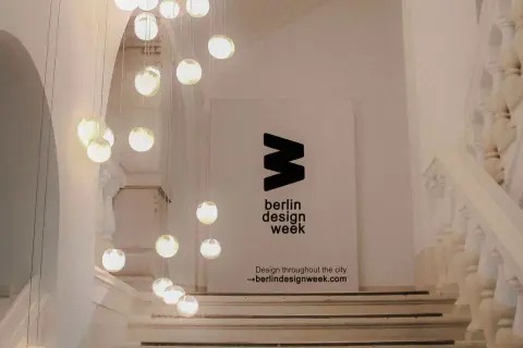 Eine Treppe mit Hängeleuchten und einem Banner für die **Berlin Design Week**.