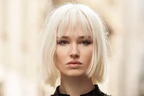 Mujer joven con un moderno corte bob rubio platino y maquillaje sutil.