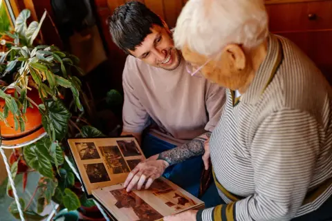 Un jeune homme et une personne âgée regardent un album photo.
