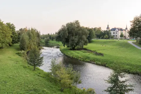 Idyllischer Flusslauf mit grünen Ufern und einem Schloss im Hintergrund. Ein perfekter Ort für Radwege Geheimtipp-Touren.